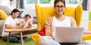 mom-in-yellow-chair-on-computer-kids-in-background-why-showing-up-in-business-can-create-huge-results-for-mompreneurs